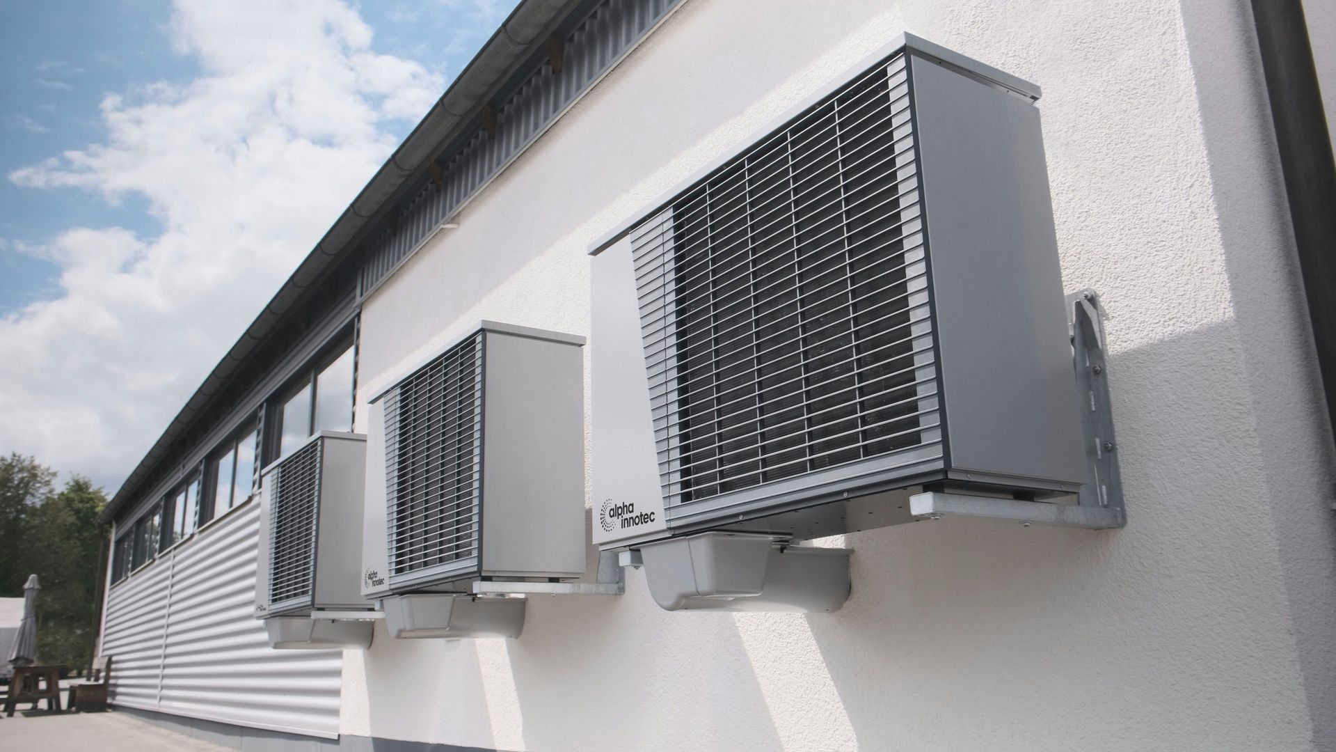Three gray air conditioning units mounted on a white wall.