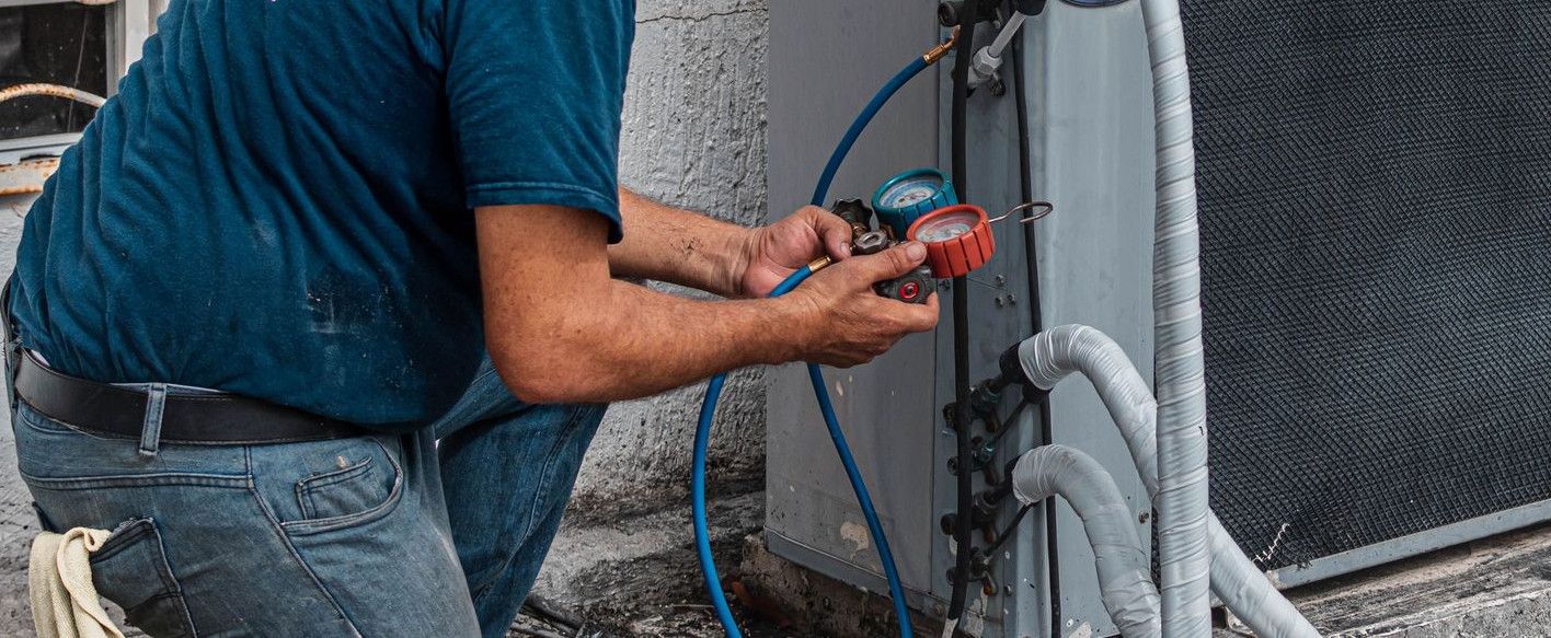 Technician repairing an air conditioner unit outdoors, wearing a facemask and using a manifold gauge.